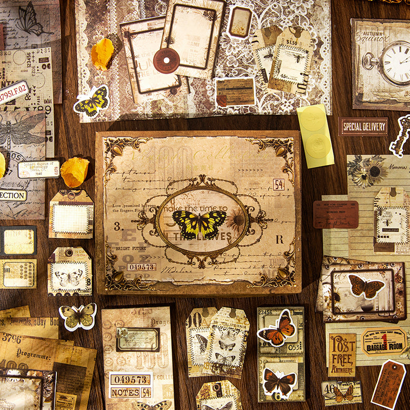 Overhead view of the complete 153-piece Curiosity Cabinet vintage journaling kit. The classic butterfly gift box is surrounded by an abundant spread of lace background papers, antique tags, and vintage butterfly stickers.
