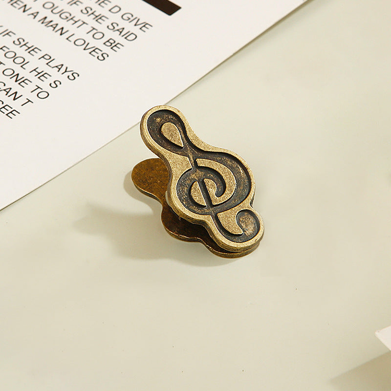 Single antique bronze treble clef metal clip securing vintage journal paper.