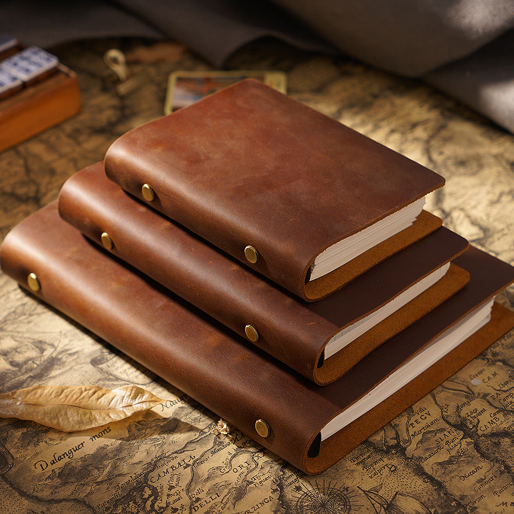 Three brown crazy horse leather ring binders in A5, A6, and A7 sizes stacked on a vintage map. Brass snap closures and natural patina visible.