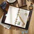 Open leather ring binder journal showing refillable blank pages and rings
