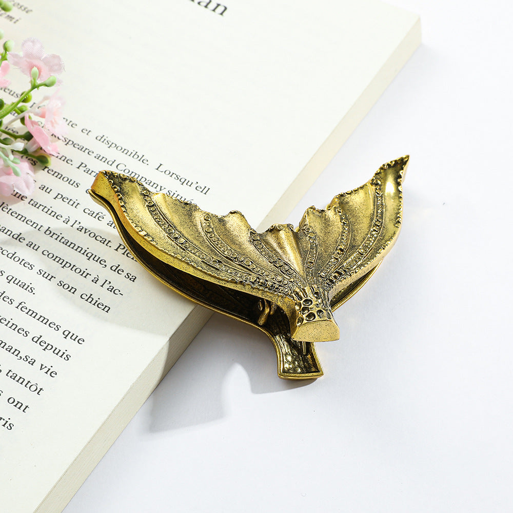 Detailed shot of an Aged Antique Brass mermaid tail metal page holder on an open book, emphasizing its retro tarnished finish and large size for thick planner spreads.