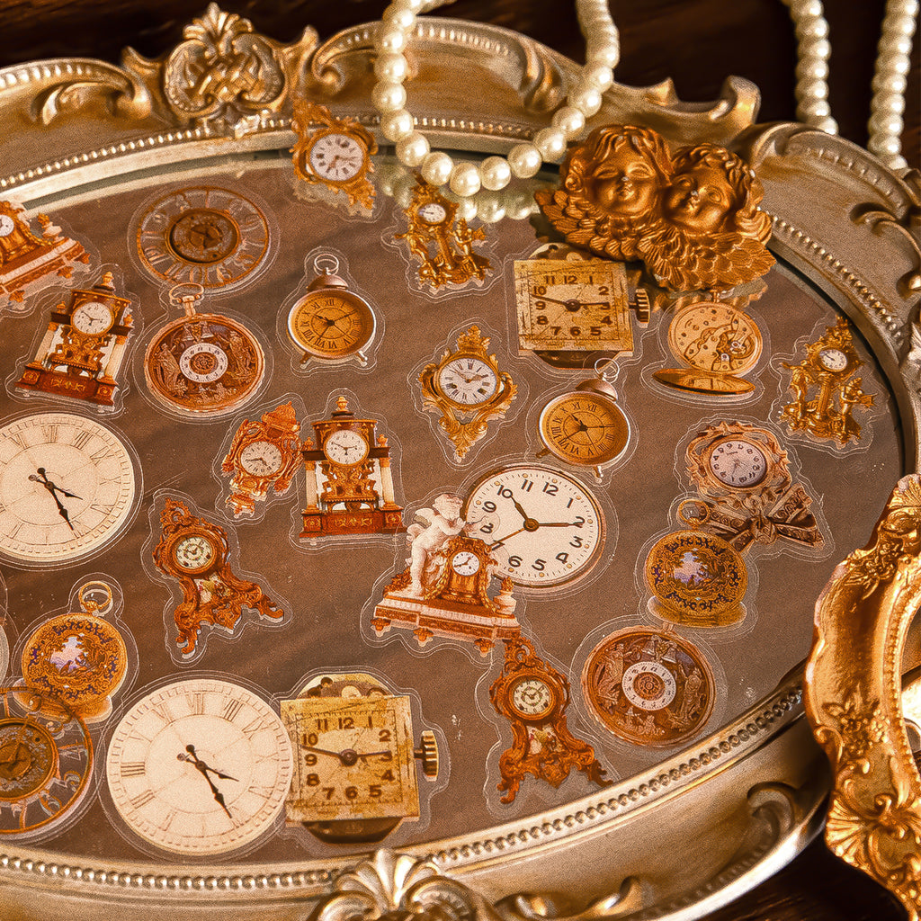 Vintage clock and timepiece PET stickers with pocket watches, mantel clocks, and Roman numerals arranged on an ornate gold tray with pearls.