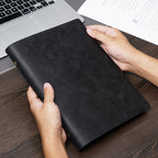 Hands holding black B5 crazy horse leather ring binder journal at laptop
