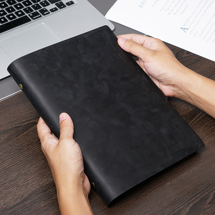 Hands holding black B5 crazy horse leather ring binder journal at laptop