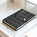 Black tweed journal lying flat on a desk, gold-thread weave detail visible