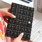 Hand holding the black tweed journal, pearl button and woven texture visible