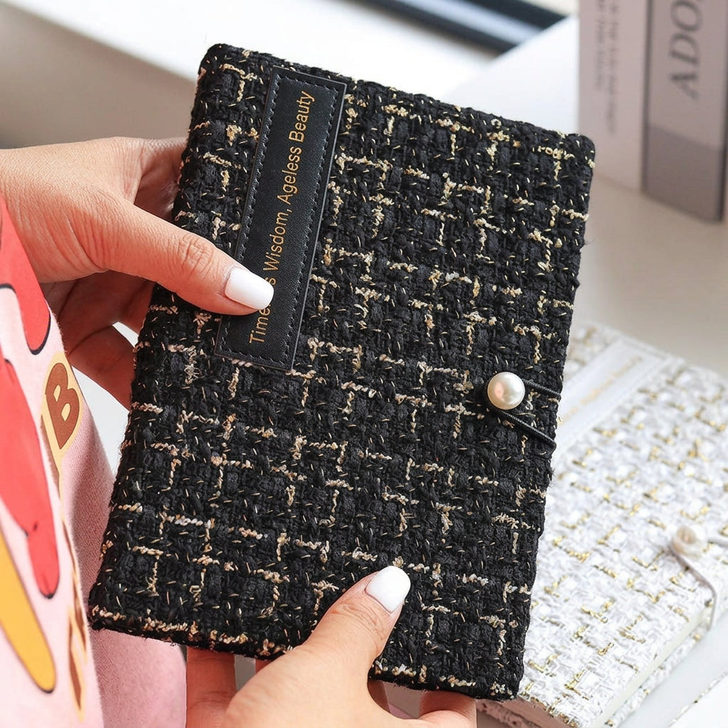 Hand holding the black tweed journal, pearl button and woven texture visible