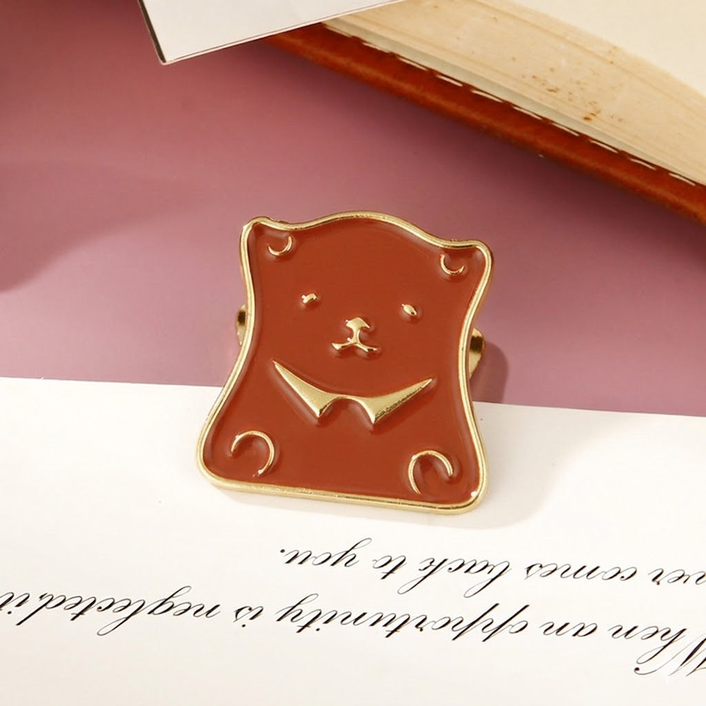 A burnished gold retro bear head metal paper clip resting against a book and letters, designed for heavy-duty planner organization and creative stationery lovers.
