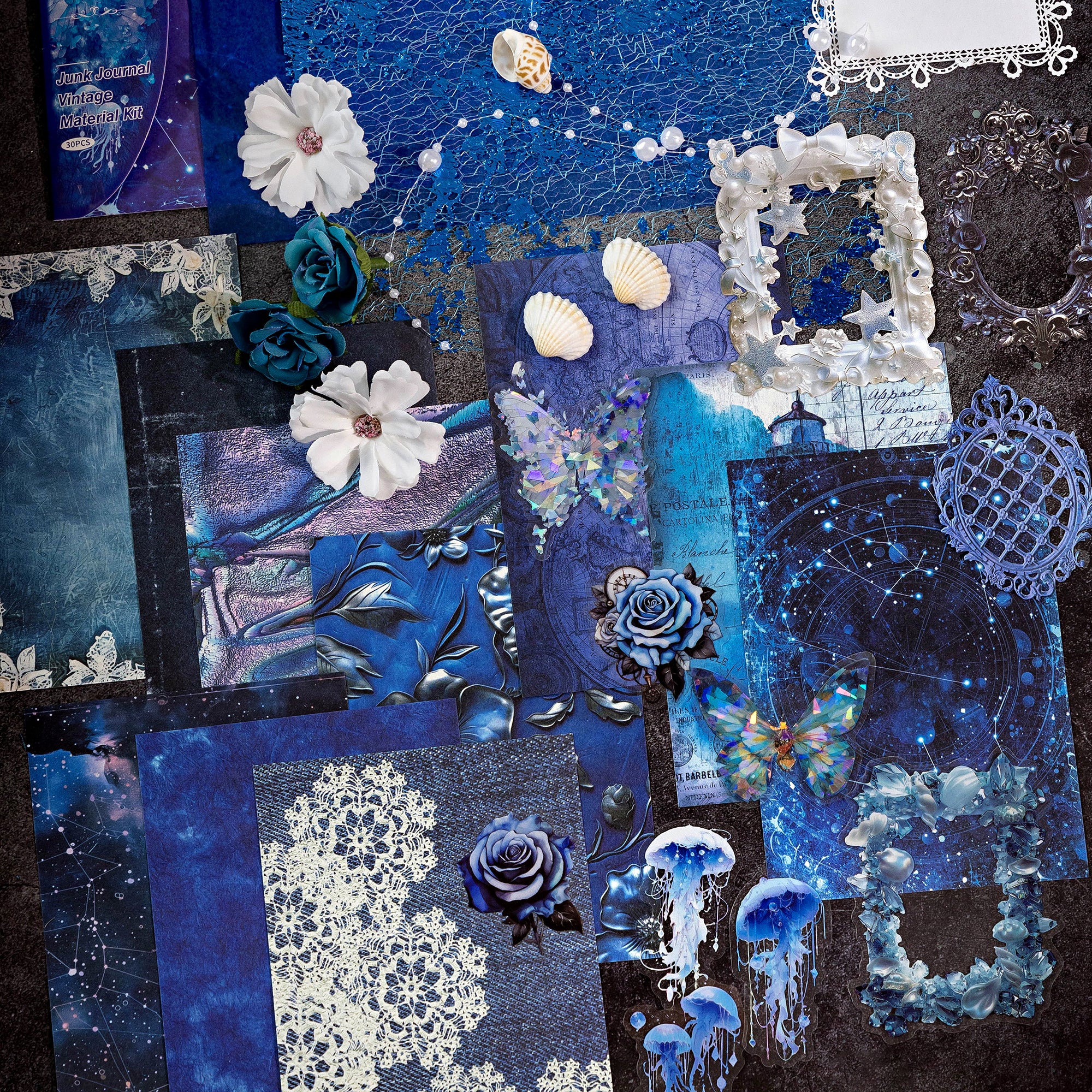 Variant image of the Celestial Ocean style Premium Mixed Media Junk Journal Kit in its blue and holographic packaging. Shows the assorted 30 pieces including the large laser-cut frame, the 'ice crystal' holographic PET butterflies and gears, and textured specialty paper through the clear window.