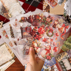 Hand holding layered vintage Christmas ephemera pile with red floral stickers and aged paper pieces