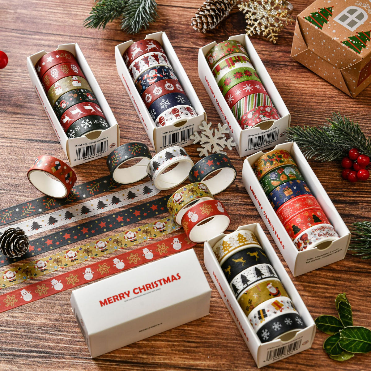 Five boxes of Christmas washi tape rolls unrolled on wooden table with pine cones