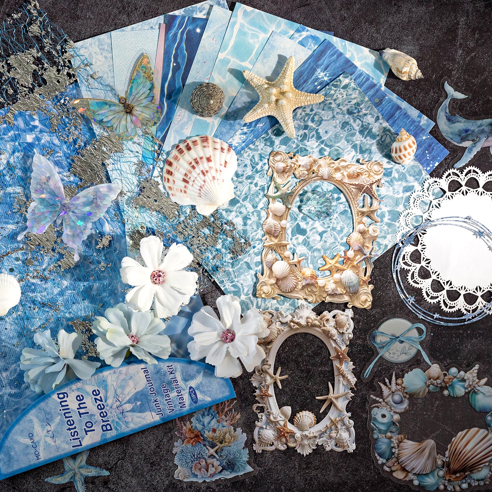 Variant image of the Coastal Whispers style Premium Mixed Media Junk Journal Kit in its light blue and white packaging. Shows the 30 coastal-themed pieces including delicate laser-cut wave frames, holographic PET seashells and lace elements, and soft textured papers.