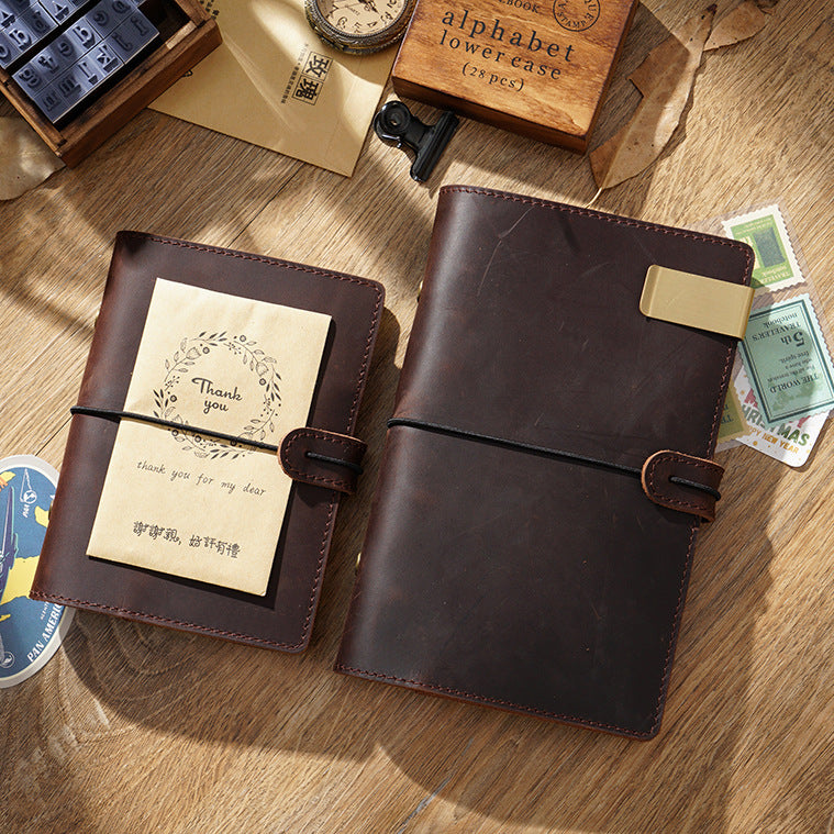 Two coffee brown leather ring binder journals stacked on wooden desk