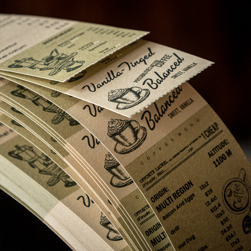 Stack of vintage coffee tear-off notepads showing vanilla balanced and process printed designs, retro cafe typography and cup illustrations on lightweight paper strips