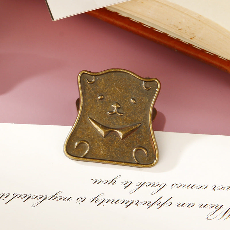 Close-up of a distressed antique bronze whimsical bear head metal clip resting on vintage manuscript paper, perfect for securing junk journals and planners.