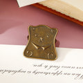 Close-up of a distressed antique bronze whimsical bear head metal clip resting on vintage manuscript paper, perfect for securing junk journals and planners.