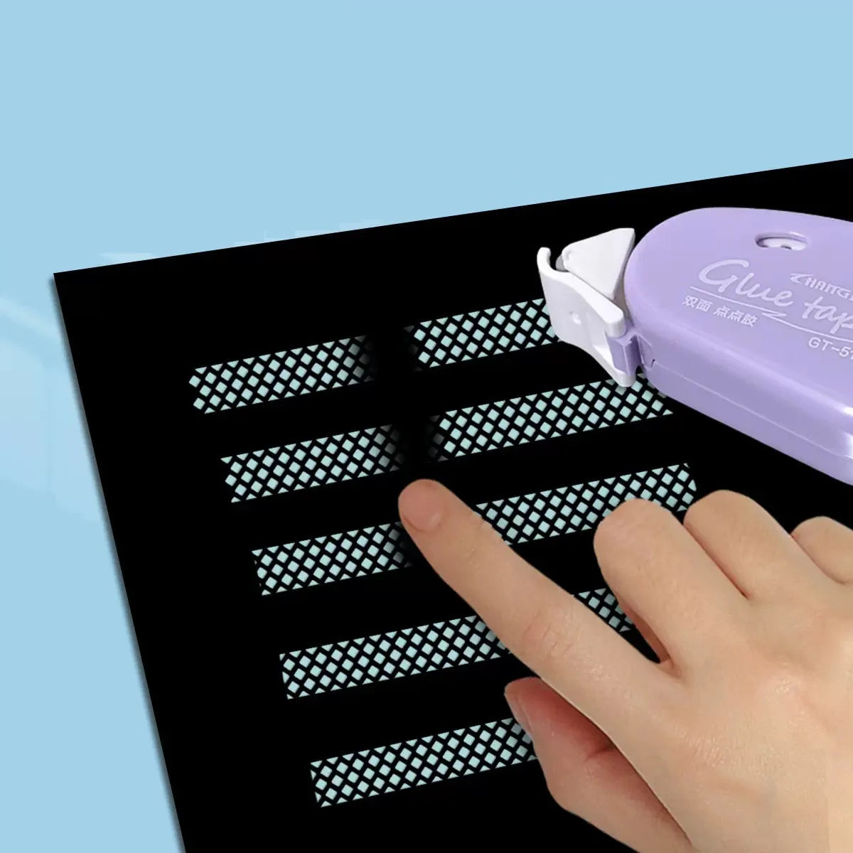 Finger pressing dot-patterned adhesive strip applied by glue tape roller on black paper