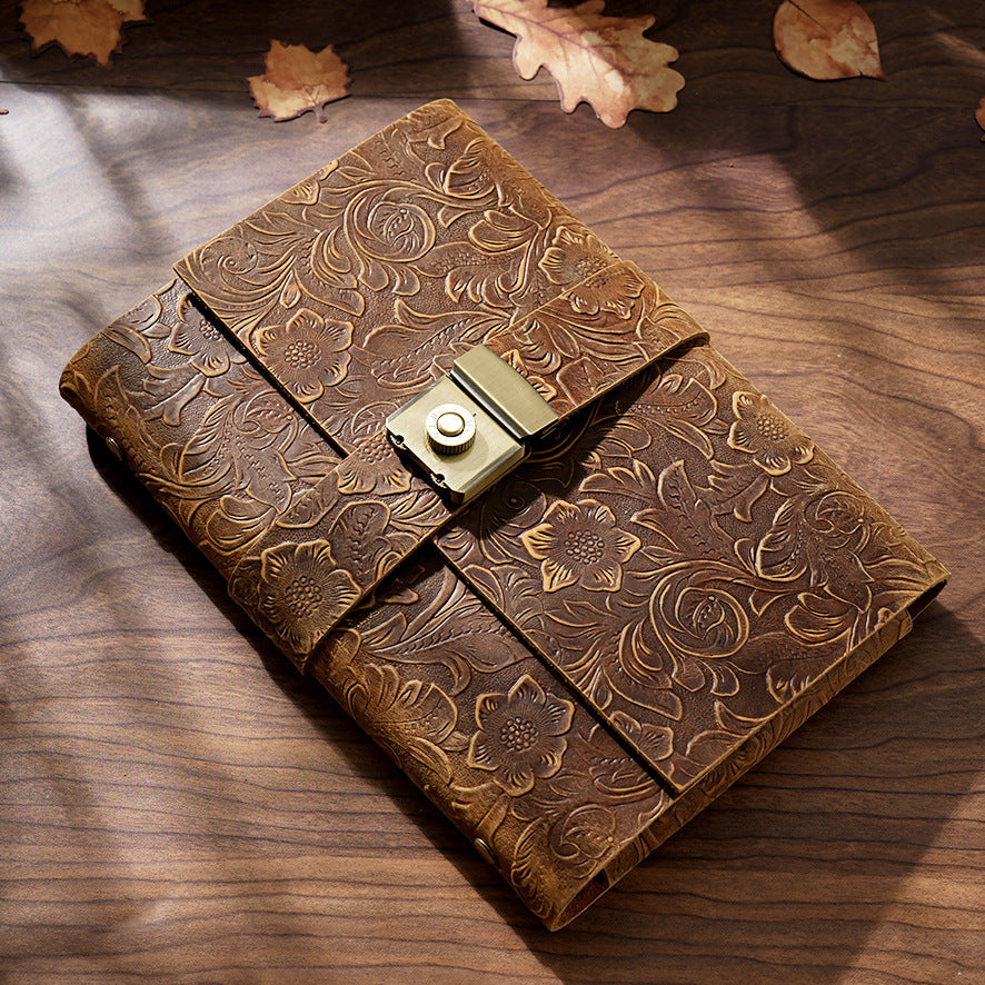 Variant image of the Embossed Antique Floral genuine crazy horse leather lock journal. Showcases intricate botanical and floral embossing on the brown top-grain leather cover, secured with a vintage metal lock, resting on a wooden desk with autumn leaves.
