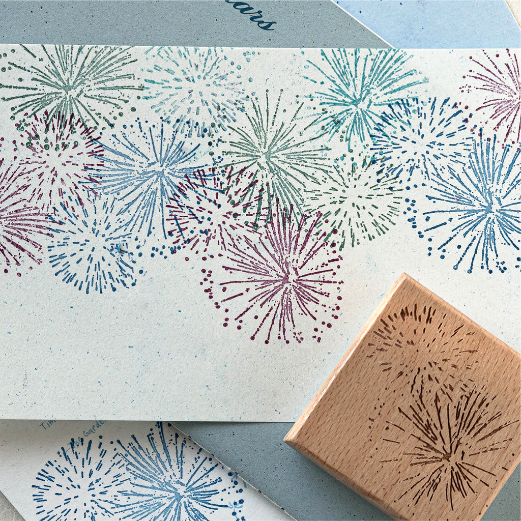 Colorful stamped impression of firework and starburst pattern on textured paper, vintage wooden rubber stamp shown in corner for journal decoration
