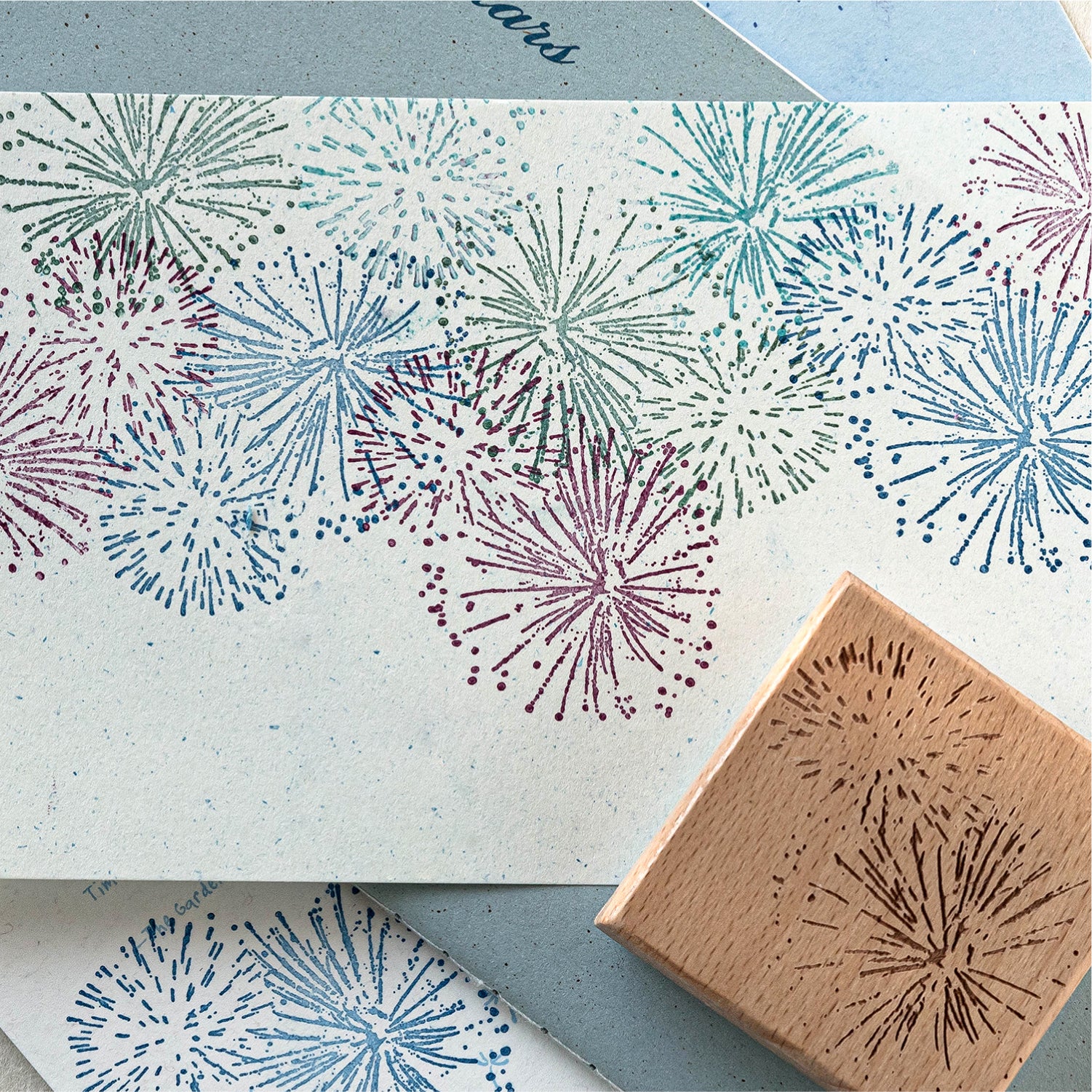 Colorful stamped impression of firework and starburst pattern on textured paper, vintage wooden rubber stamp shown in corner for journal decoration