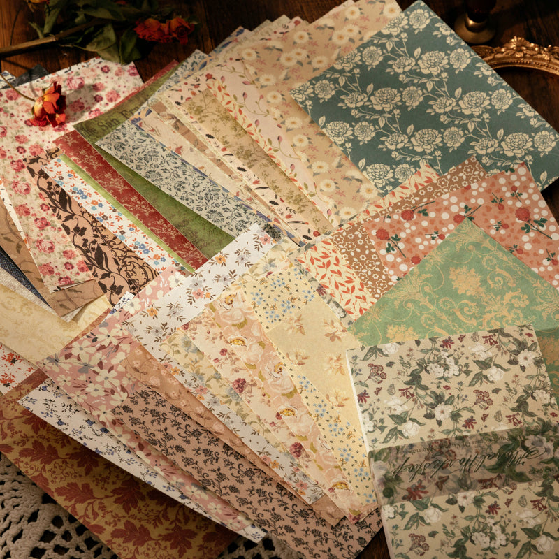 Assorted floral scrapbook paper sheets fanned on a wooden surface, featuring botanical prints, pressed flowers, and vintage garden patterns.
