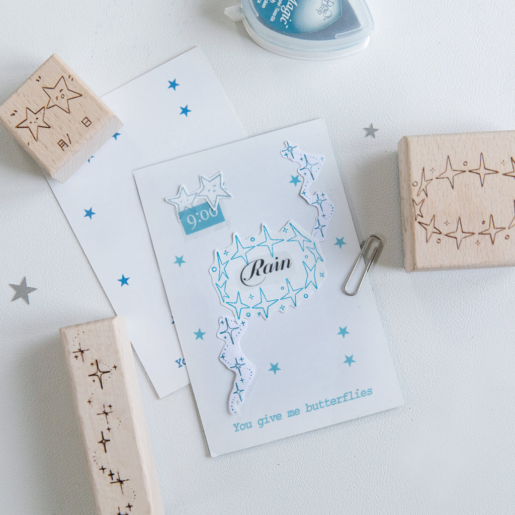 Vintage star beech wood rubber stamps in use with blue constellation impressions on white paper, star face date stamp and star trail border stamps, pre-cut celestial carved rubber stamps for journal decoration