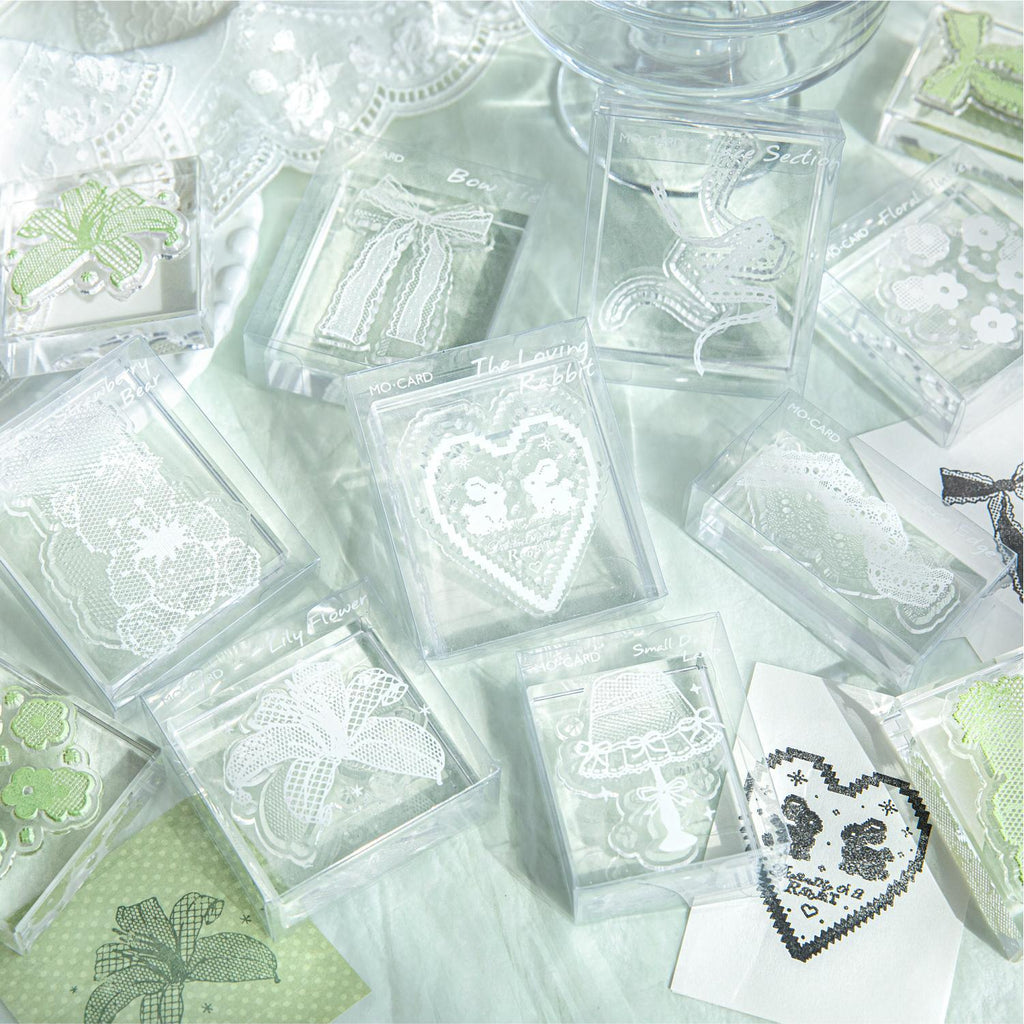 Clear acrylic stamps with lace heart motif arranged on soft green fabric with stamped impressions