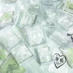 Clear acrylic stamps with lace heart motif arranged on soft green fabric with stamped impressions