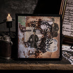  A framed junk journal collage artwork featuring vintage character stickers, ornate black lace cutouts, and distressed paper layers, displayed beside a lit candle and antique camera.