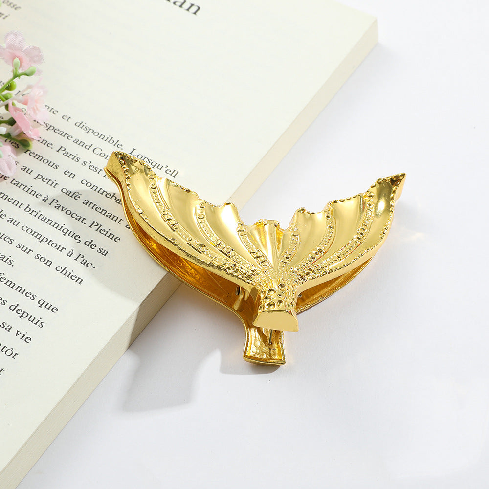 Close-up of a Luminous Siren Gold vintage mermaid tail journal clip securing the pages of a book, highlighting its heavy-duty build and radiant nautical aesthetic.