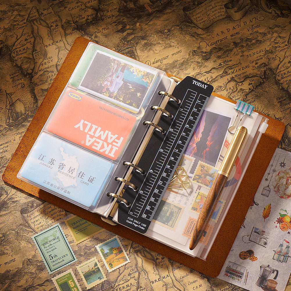 Open A5 crazy horse leather ring binder showing 6-ring mechanism, card slots, ruler insert, and fountain pen on vintage map paper.