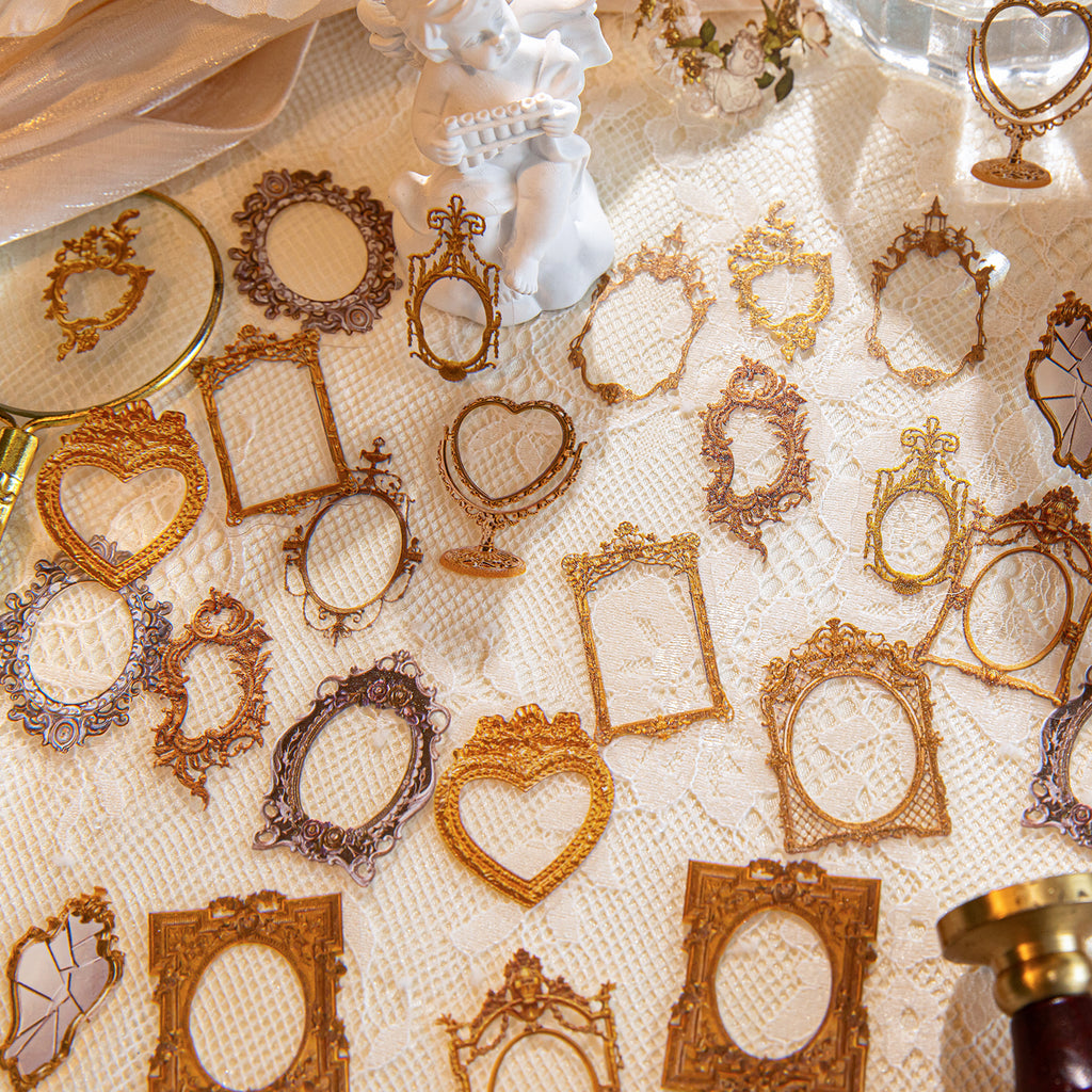 Assorted vintage gold frame PET stickers in round, heart, and crown shapes scattered on white lace with a small cherub figurine.