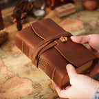 Hands holding pocket hand-stitched leather sketchbook with cord closure on vintage map