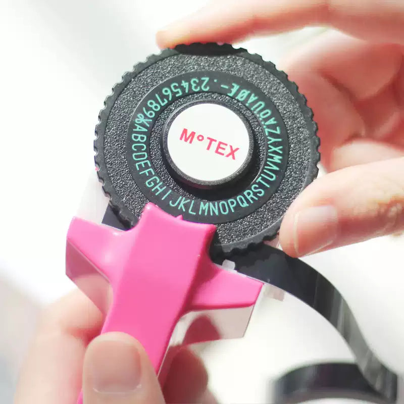 Hand holding a pink embossing label maker with letter dial