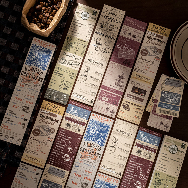 All six vintage coffee notepad designs fanned out on dark surface with coffee beans, showing almond croissant, city roast, floral brand, and colombian bread cafe ephemera prints