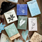 Vintage wooden rubber stamp collection with printed packaging cards showing lily flower shadow, ink colored fireworks, raindrops ripples, and butterfly dances designs