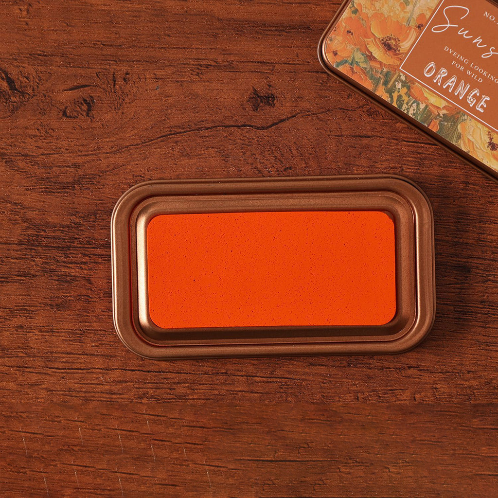 Vintage iron box ink pad in Sunset Orange open on wood, orange sunset lid beside