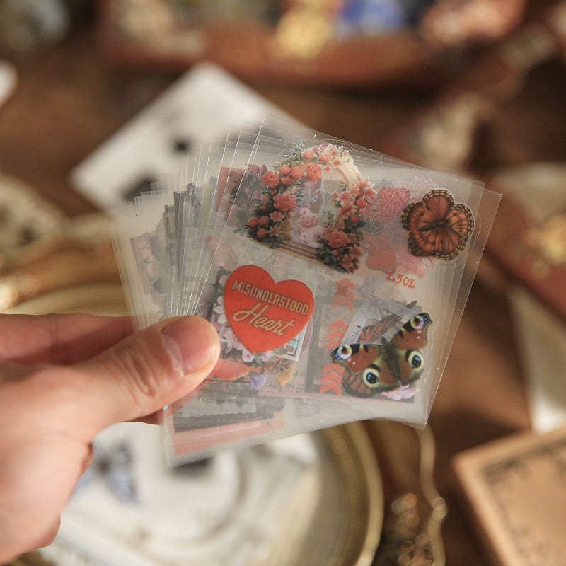 Image of transparent PET vintage stickers fanned out showing heart shape, red butterfly, and floral designs, clear waterproof layering pieces for scrapbook spreads
