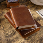 Two brown crazy horse leather A5 notebooks stacked at an angle, showing brass edge snaps, thick paper stack, and soft leather cover texture.