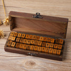 Open wooden keepsake box of vintage alphabet stamps beside dried flowers on desk