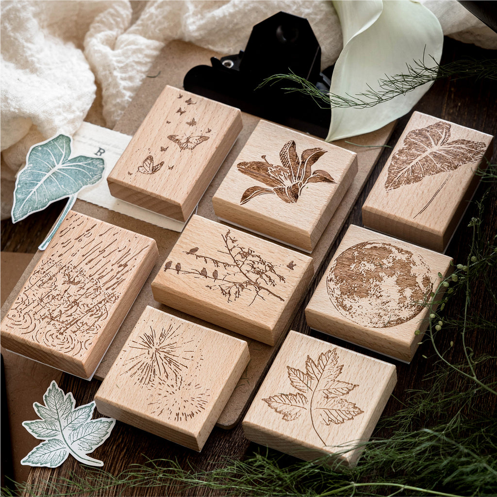 Vintage beech wood rubber stamps scattered on natural surface with carved botanical and butterfly designs, wooden base with detailed rubber surface for journaling