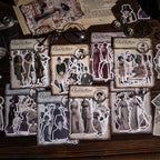  Eight vintage character sticker packs arranged on a wooden desk with antique glasses, pocket watches, and aged newspaper pages. Each pack displays die-cut sepia portraits in Victorian and Edwardian dress.