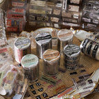 Six vintage ephemera PET tape rolls arranged on aged newspaper with candlelight and dried flowers showing newspaper clipping and burnt diary designs