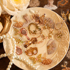 Scattered vintage gilded PET stickers with ballet dresses, crowns, mirrors, and fans arranged on an ornate white porcelain plate with pearls.