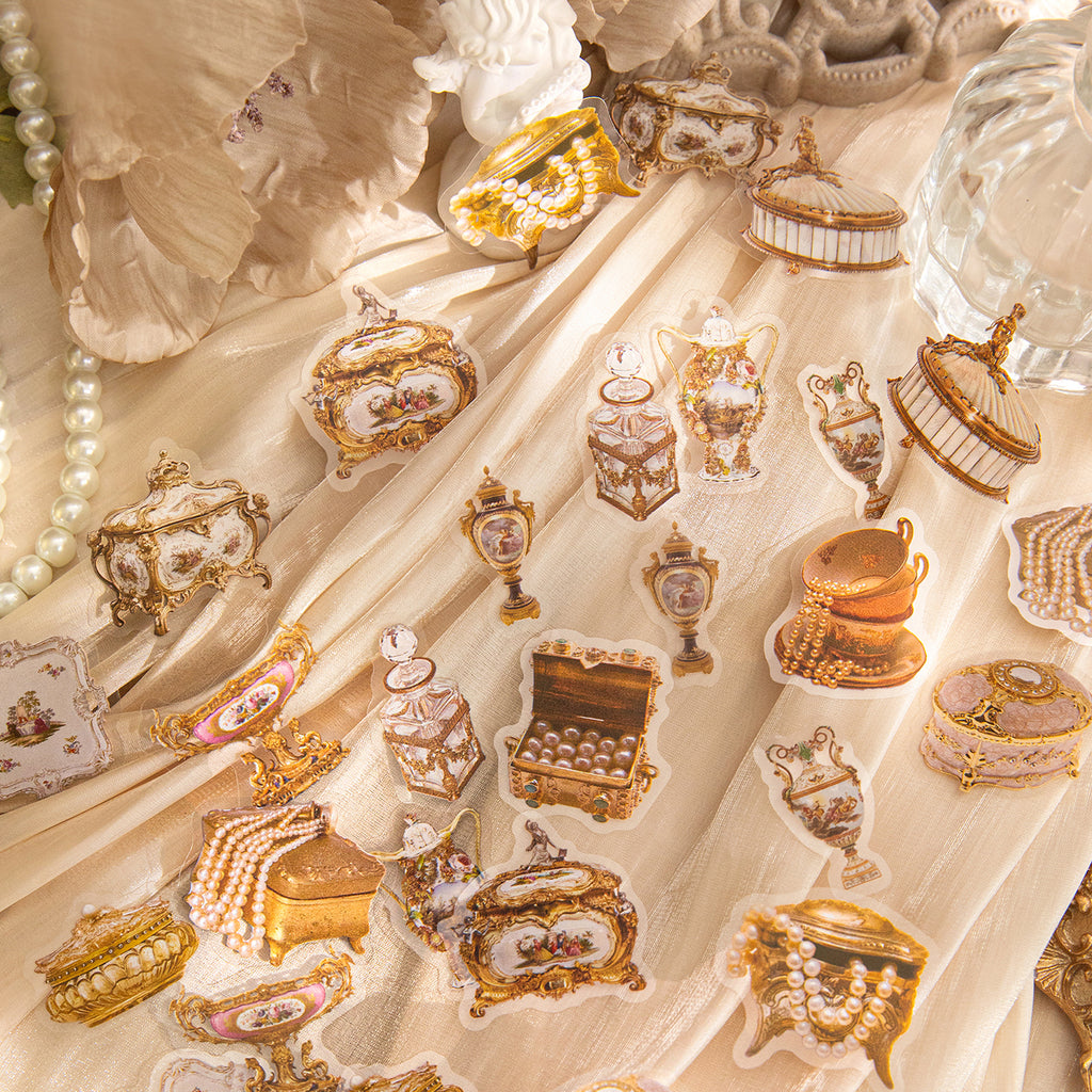 Vintage gilded PET stickers with ornate jewelry boxes, perfume bottles, teapots, and pearl necklaces scattered on cream silk fabric.