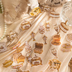 Vintage gilded PET stickers with ornate jewelry boxes, perfume bottles, teapots, and pearl necklaces scattered on cream silk fabric.