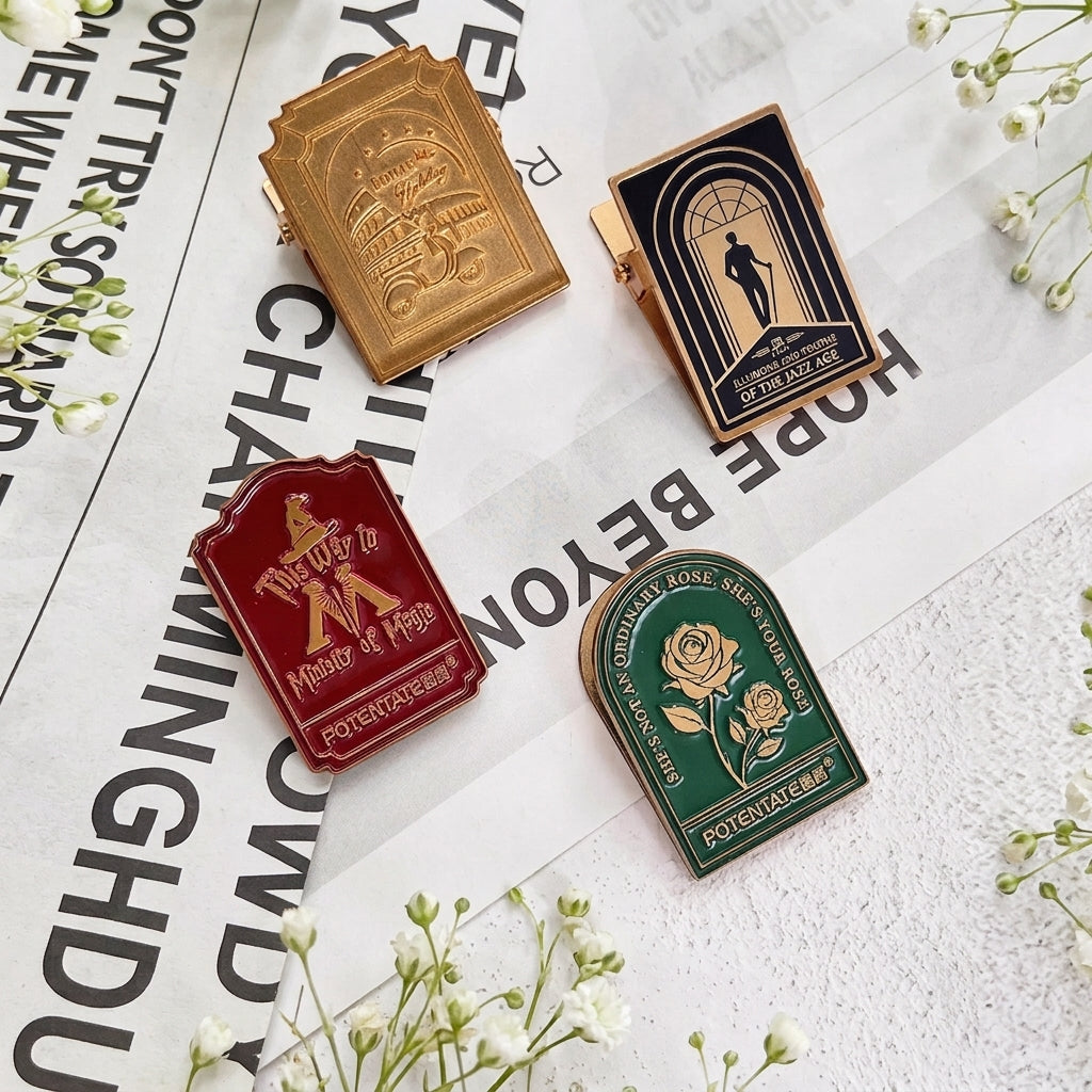 Four vintage zinc alloy binder clips with embossed enamel designs in gold, black, red and green