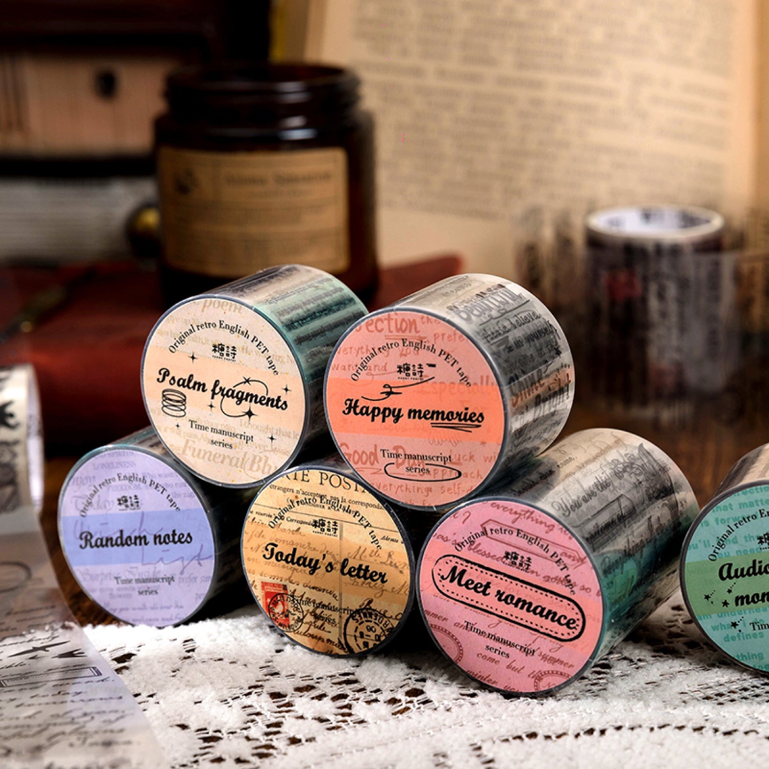 Six vintage script PET tape rolls displayed upright with colorful printed labels showing assorted English themes and titles.