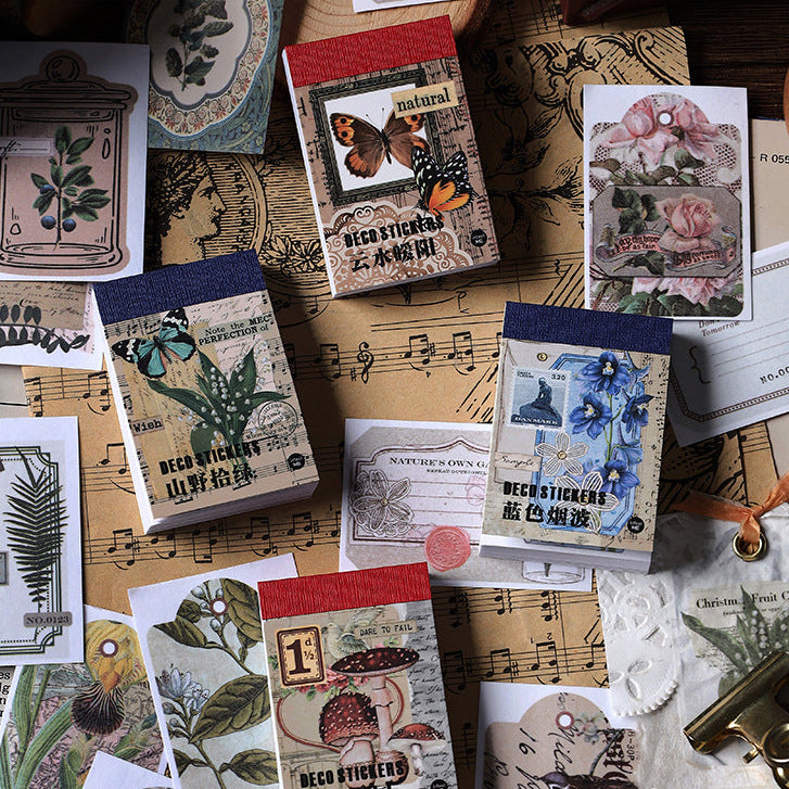 Four vintage washi sticker books displayed on rustic kraft paper with botanical sheet music, fern leaves, and antique stamp decorations, showcasing woodland and nature-themed illustrations