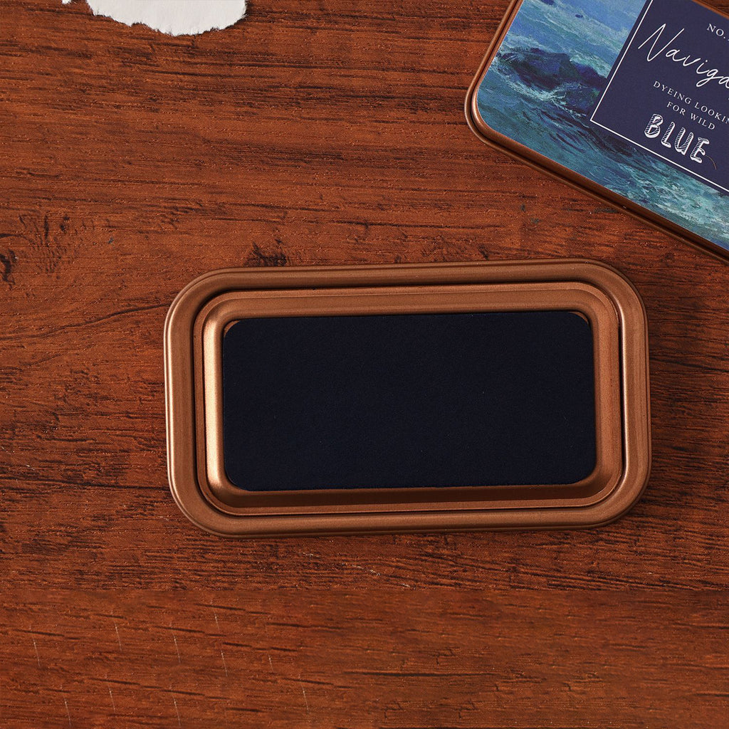 Vintage iron box ink pad in Voyage Blue open on wood, navy sea lid beside